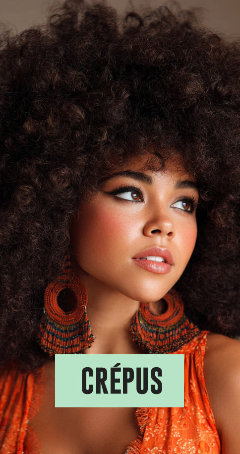 Close-up of a woman with voluminous curly hair, wearing large orange woven earrings and an orange top, looking away.
