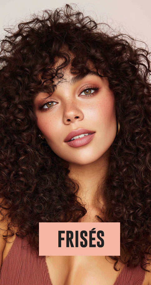 Close-up of woman with dense, voluminous dark curly hair and warm makeup, looking directly at the camera